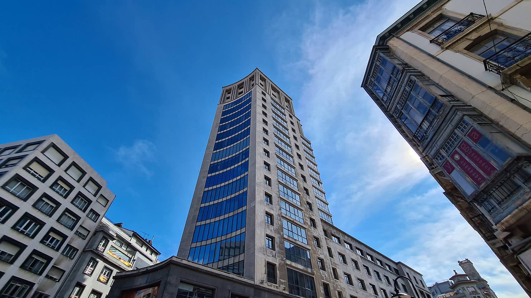 Foto en contrapicado del emblemático rascacielos la Jirafa, adaptándose la planta del edificio a la confluencia de las calles, se trata de un edificio ennoblecido, elegante, obrio y gris a caballo entre el clasicismo y la modernidad.