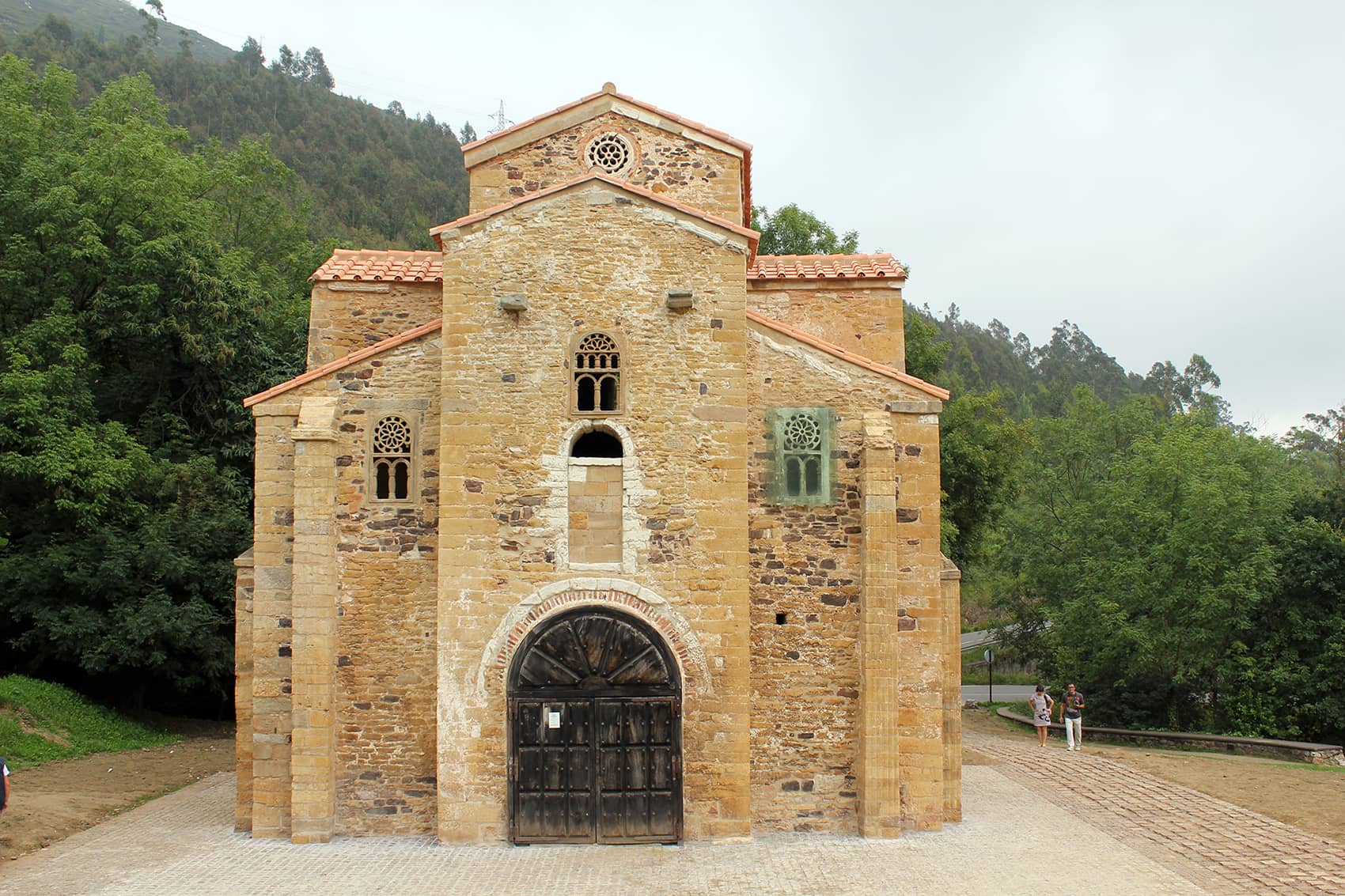 Fotografía con perspectiva frontal de la iglesia prerrománica de San Miguel de Lillo, se puede observar el pórtico central y los contrafuertes, además de la puerta de mandera entallada.